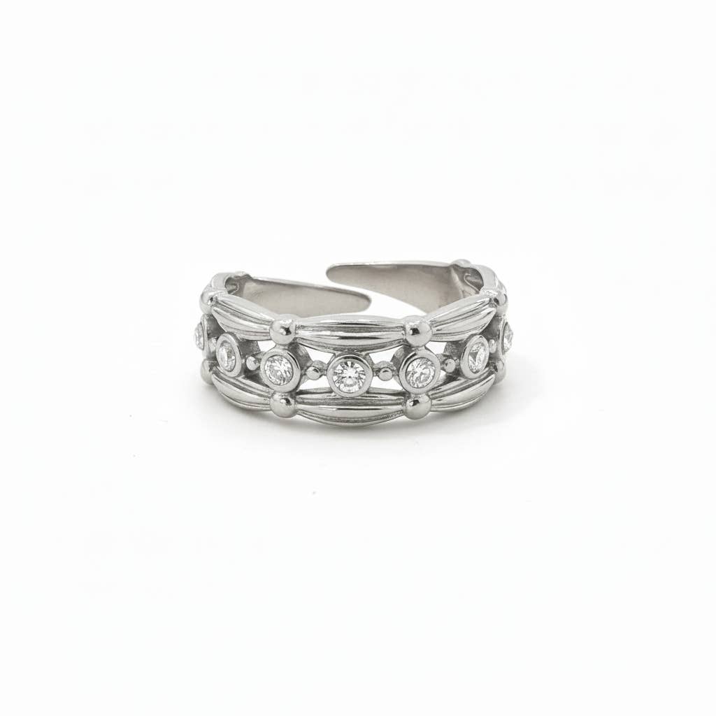 Bague large et ajustable en acier inoxydable argenté, dotée d'une rangée centrale d'oxydes de zirconium ronds et brillants encadrés par des bordures finement sculptées, isolée sur un fond blanc épuré.