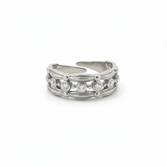 Bague large et ajustable en acier inoxydable argenté, dotée d'une rangée centrale d'oxydes de zirconium ronds et brillants encadrés par des bordures finement sculptées, isolée sur un fond blanc épuré.