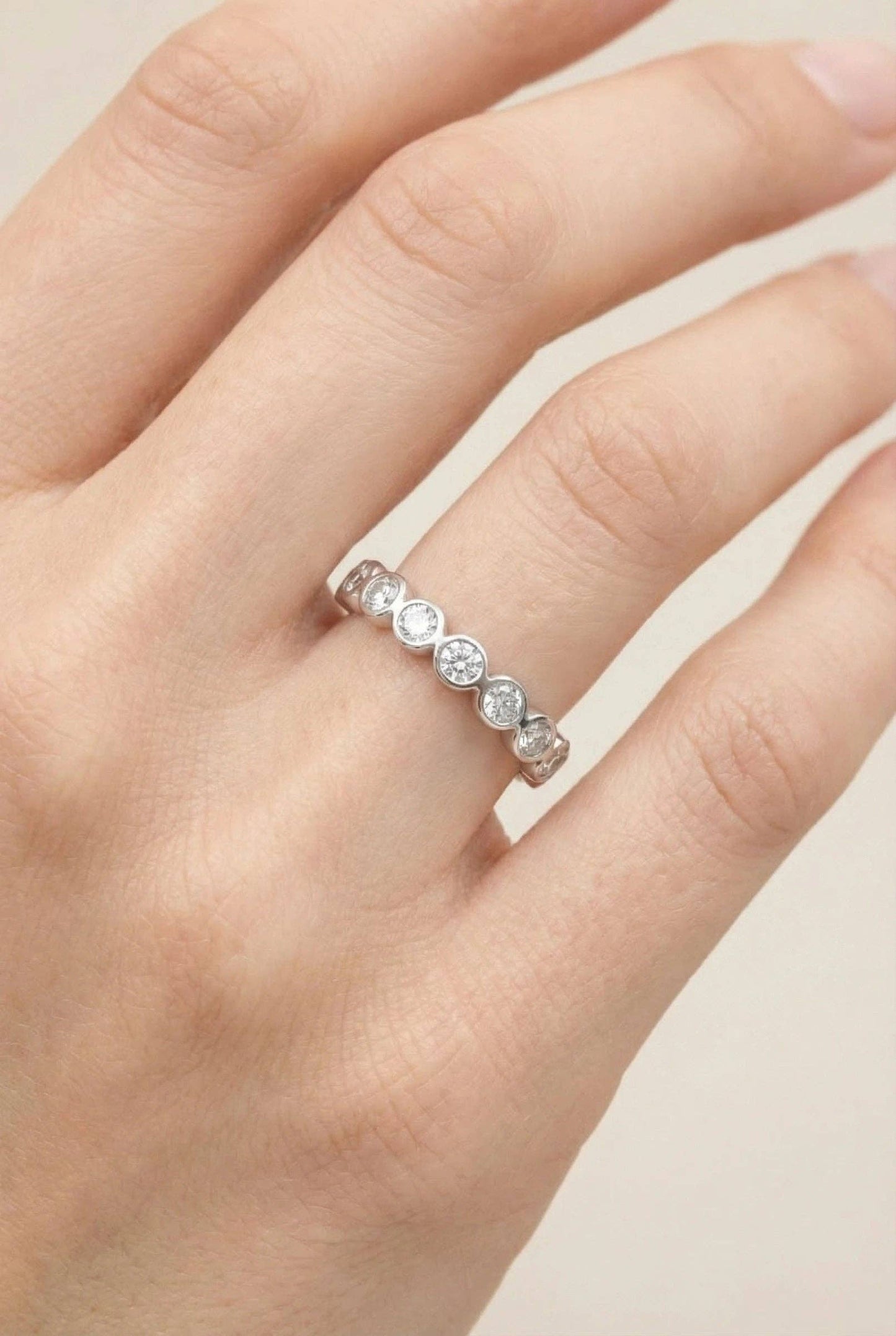 Alliance fine en acier inoxydable argenté ornée d'une suite de cristaux ronds brillants en serti clos, portée à l'annulaire d'une main de femme.