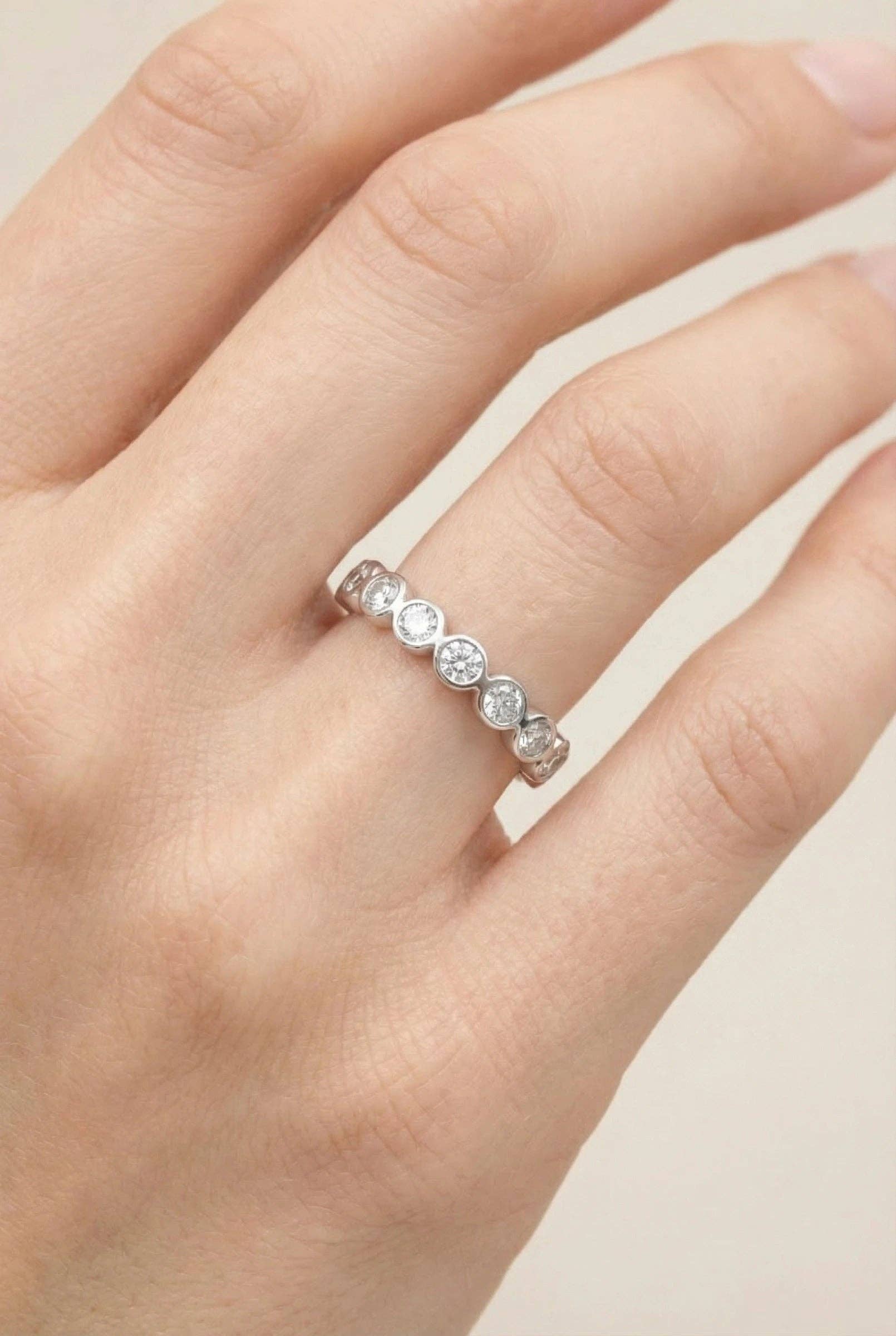 Alliance fine en acier inoxydable argenté ornée d'une suite de cristaux ronds brillants en serti clos, portée à l'annulaire d'une main de femme.