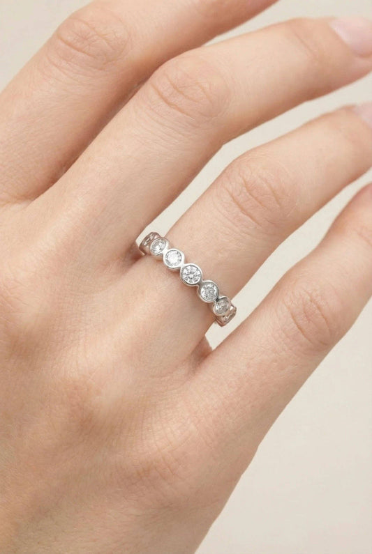 Alliance fine en acier inoxydable argenté ornée d'une suite de cristaux ronds brillants en serti clos, portée à l'annulaire d'une main de femme.