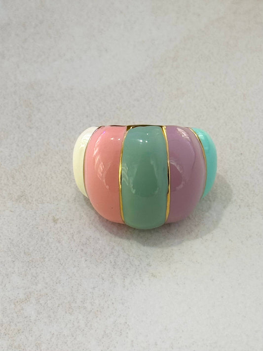 Bague large de style dôme en acier inoxydable doré, ornée de larges bandes verticales lisses en émail de couleurs pastel (crème, rose, vert sauge, lilas, turquoise) séparées par de fins filets d'or poli, présentée de face sur un fond texturé clair.
