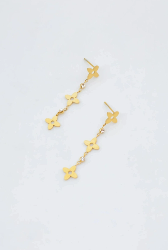 Paire de boucles d'oreilles pendantes de style clou en acier inoxydable doré, composées d'une chaîne alternant trois fleurs à quatre pétales ajourées et des petits strass brillants.