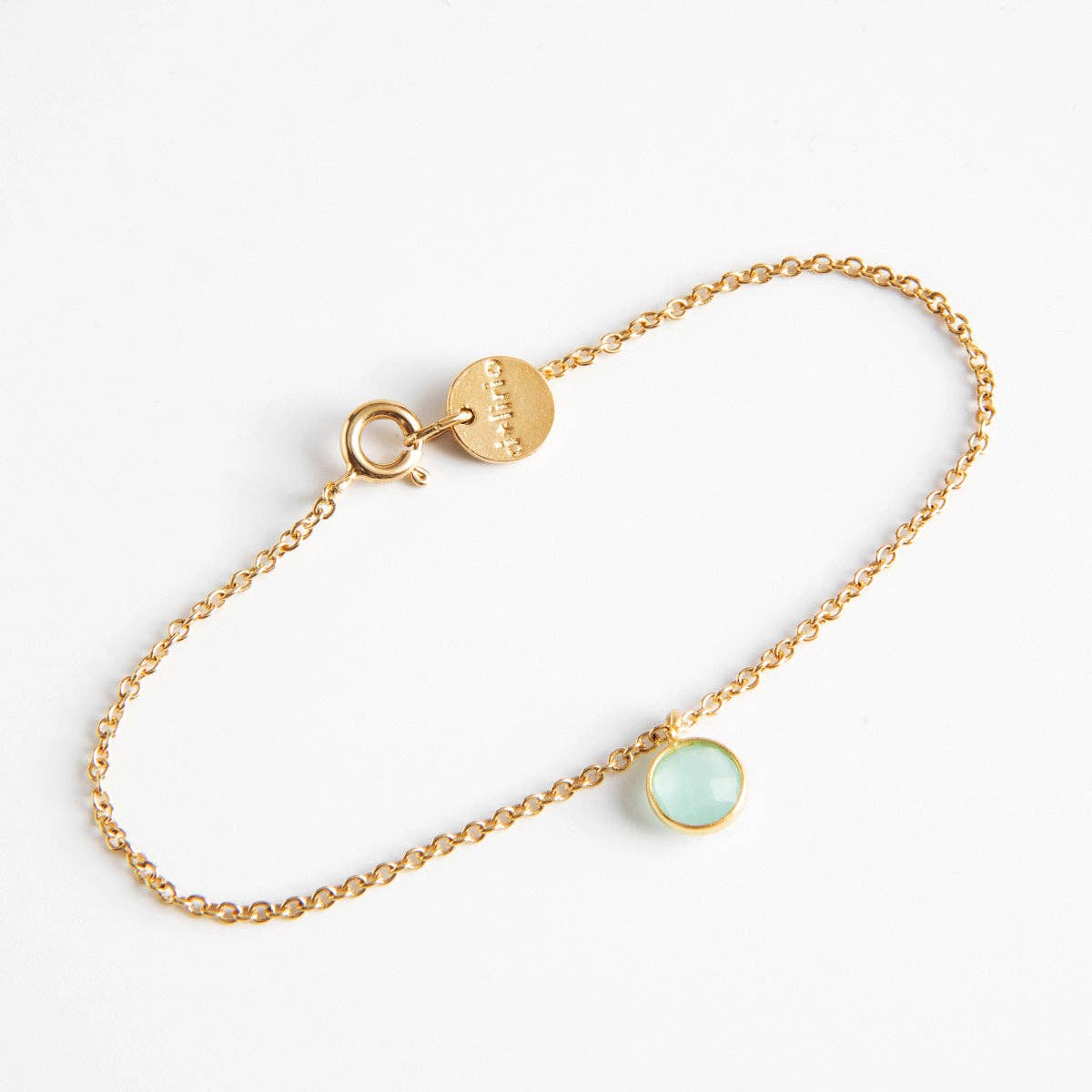 Bracelet doré fin pour femme en maille forçat avec fermoir à ressort, médaille ronde et mini pendentif rond serti clos couleur bleu aigue-marine translucide.