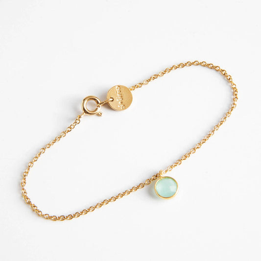 Bracelet doré fin pour femme en maille forçat avec fermoir à ressort, médaille ronde et mini pendentif rond serti clos couleur bleu aigue-marine translucide.