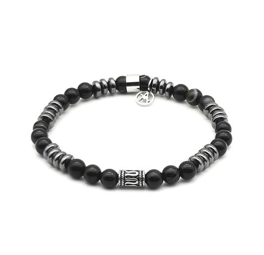 Bracelet élastique pour homme composé de perles rondes en agate noire onyx brillante, espacées par des disques en hématite métallique gris foncé, avec un intercalaire central cylindrique en acier sculpté et une breloque logo de la marque.