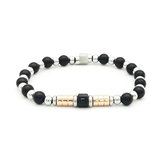 Bracelet pour homme composé de perles rondes en onyx noir brillant alternées avec des billes en acier argenté, orné de cylindres striés or rose, d'un cube noir central serti d'un strass et d'un fermoir magnétique.
