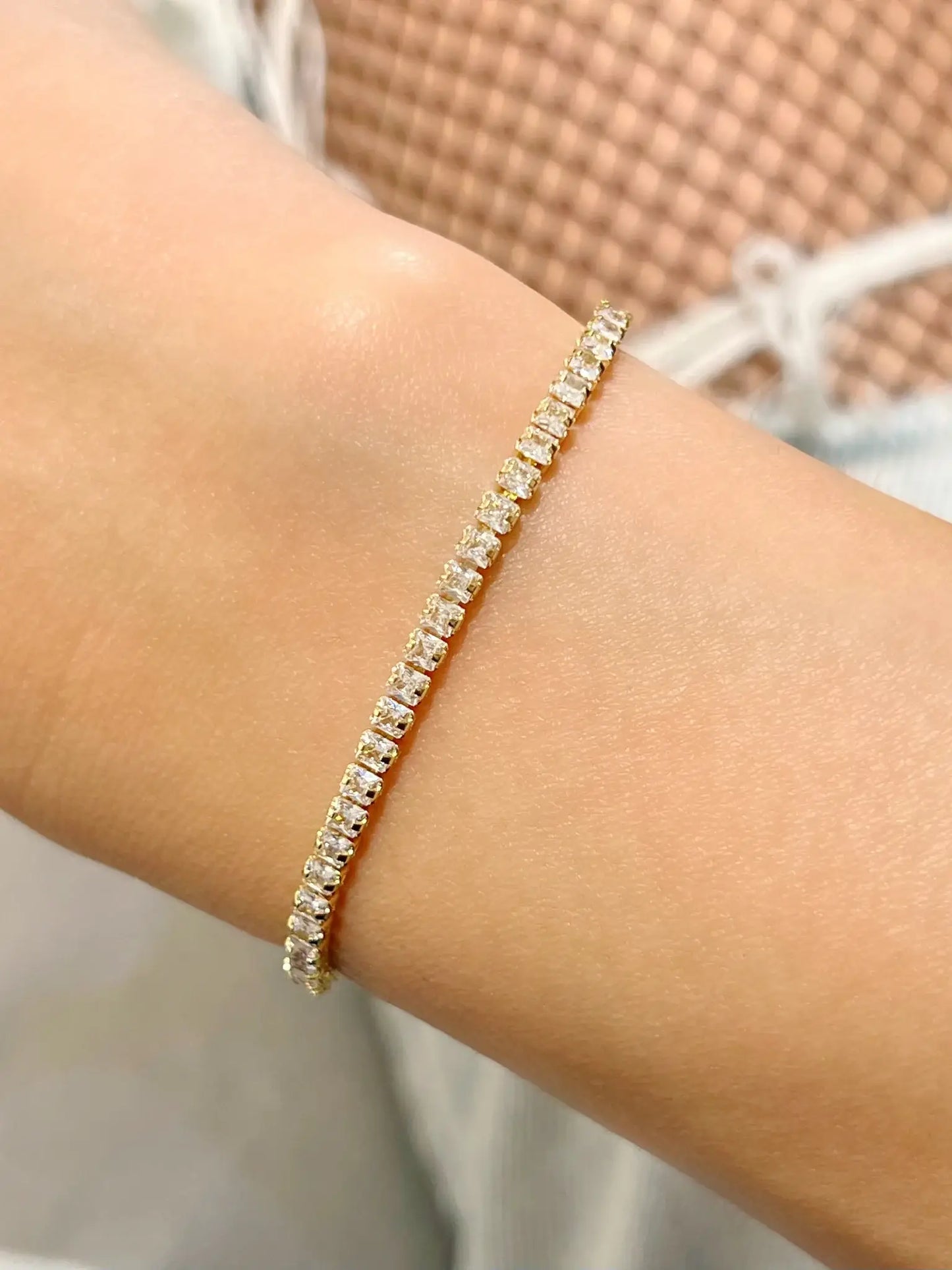 Bracelet de style rivière ou tennis en acier inoxydable doré, composé d'une ligne continue et serrée d'oxydes de zirconium carrés blancs et étincelants, porté au poignet d'une femme.