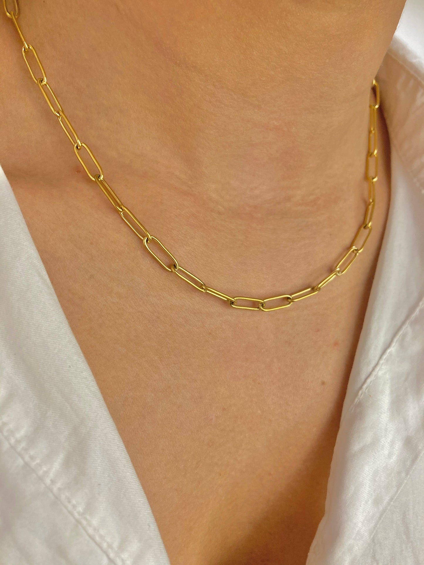 Collier à maille trombone en acier inoxydable doré, porté au cou sur un décolleté avec une chemise blanche entrouverte.