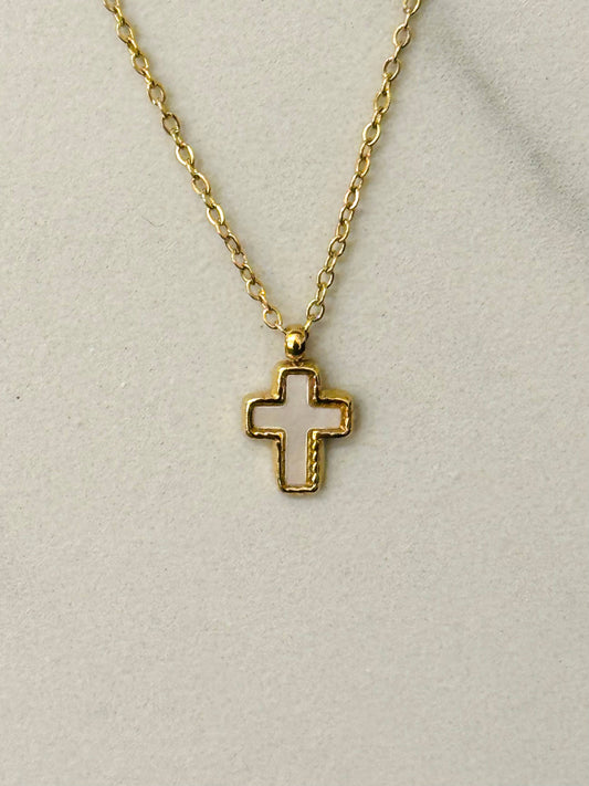 Gros plan sur un collier en acier inoxydable doré avec une fine chaîne et un pendentif petite croix orné d'un cœur en nacre blanche irisée, posé à plat.