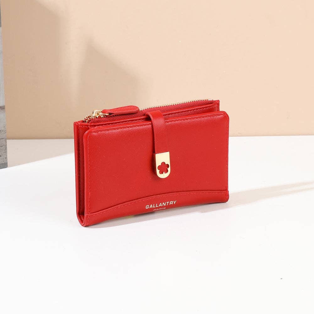 Portefeuille compact Gallantry Paris Ruby de couleur rouge vif (REF 31), en similicuir lisse avec une sangle avant à clip métallique doré en forme de trèfle ajouré, fermeture éclair dorée et inscription logo, photographié de trois-quarts sur une table blanche.